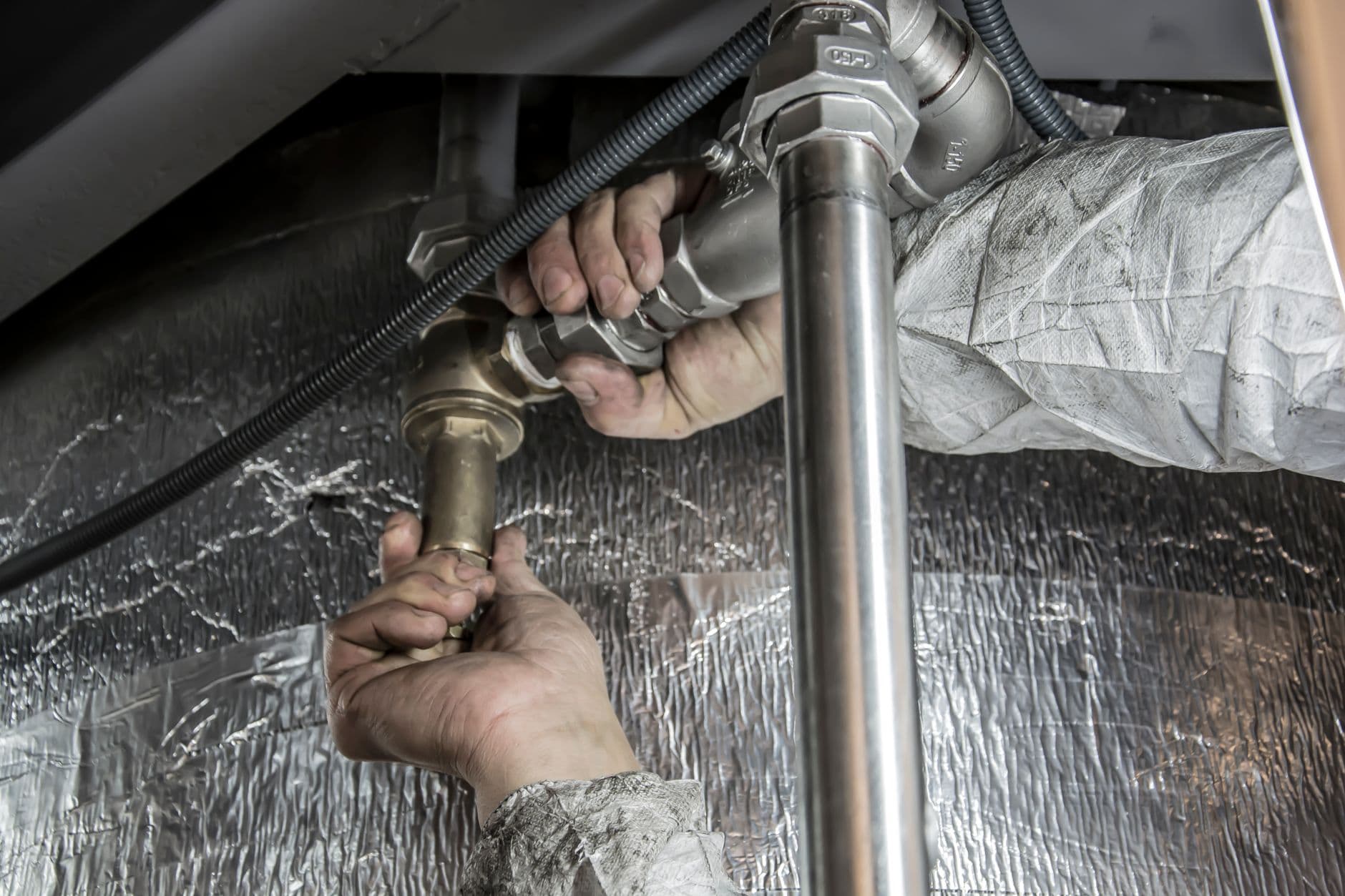A plumber's hands fitting drain pipework under a fixture