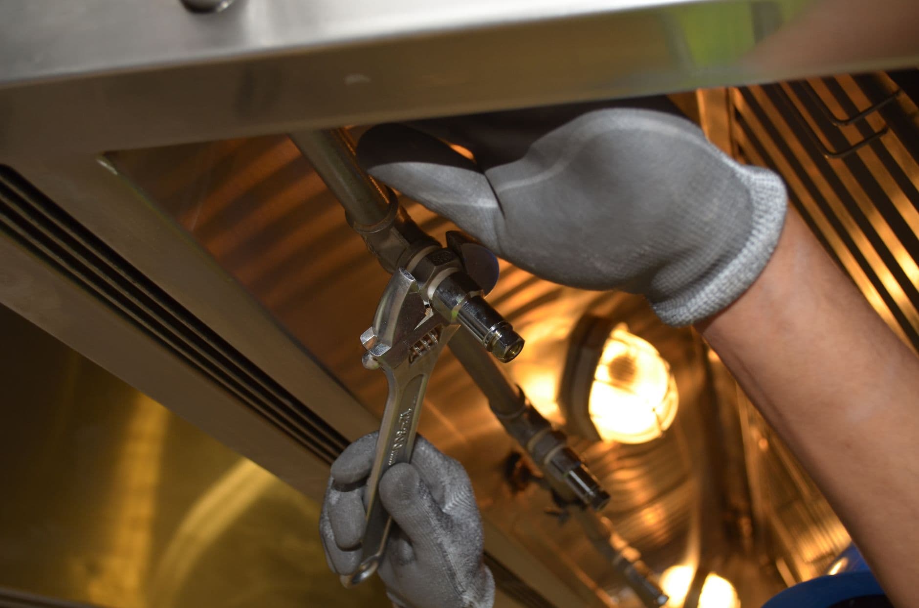 A plumber's gloved hands tightening a fixture valve with a wrench