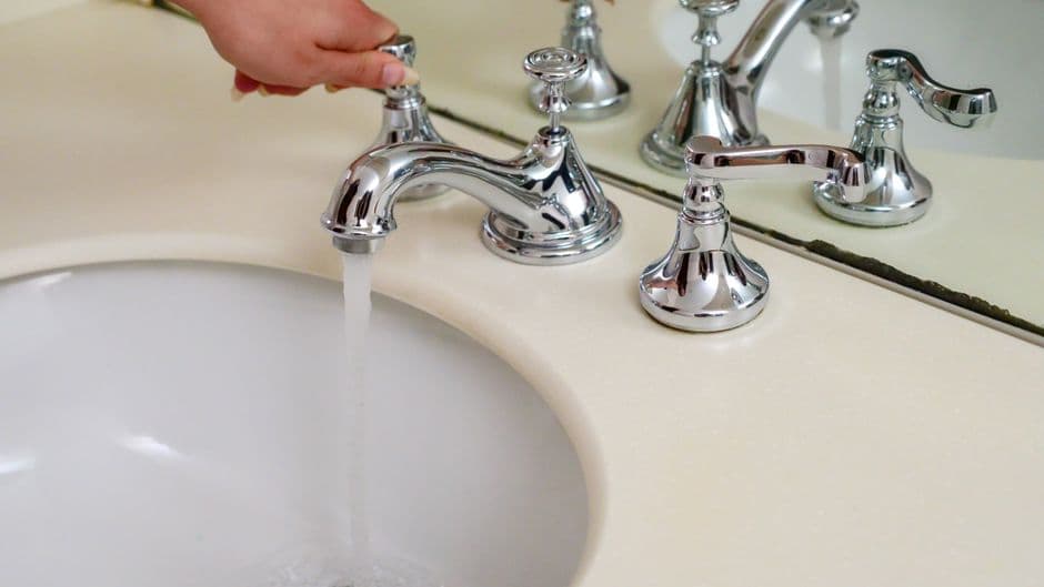 A hand operating a chrome faucet with running water