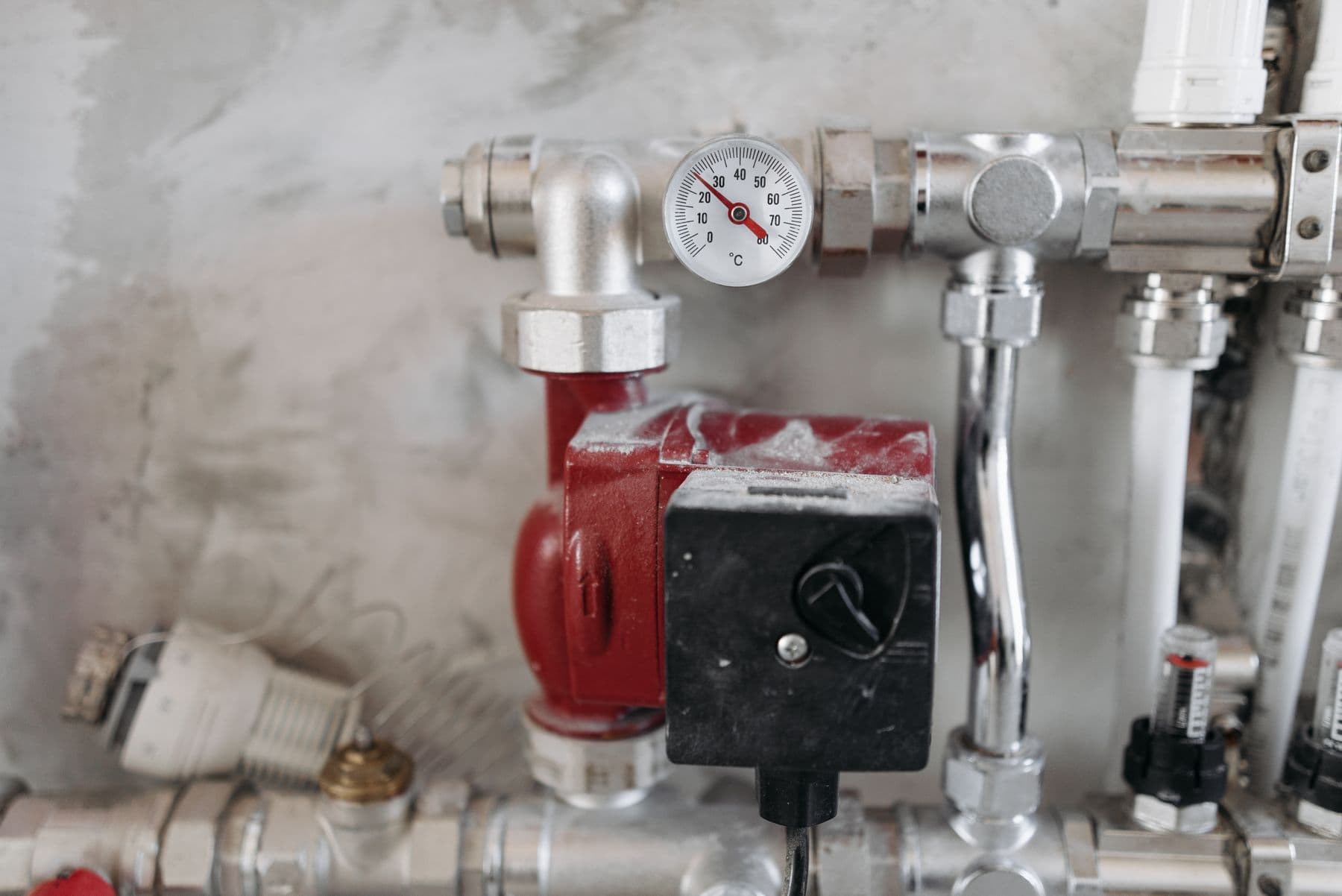 A heating system's red circulation pump, pressure gauge, and steel pipework